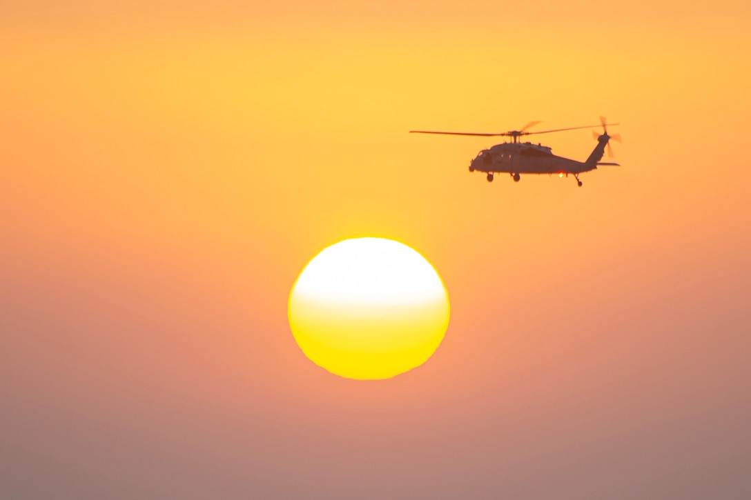 A helicopter flies in the sky; the sun seen below.