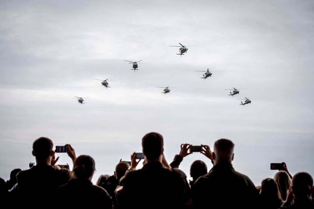 Spectators look up to the sky as a group of helicopters fly.