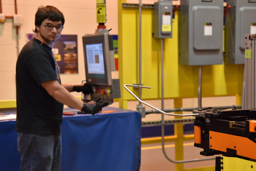 Photo shows male using a machine to bend a metal cable.