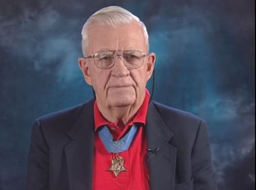 An older gentleman wearing a Medal of Honor looks into a camera.