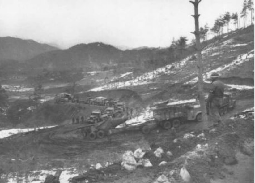 Military vehicles follow zig-zagged muddy roads up a hill.