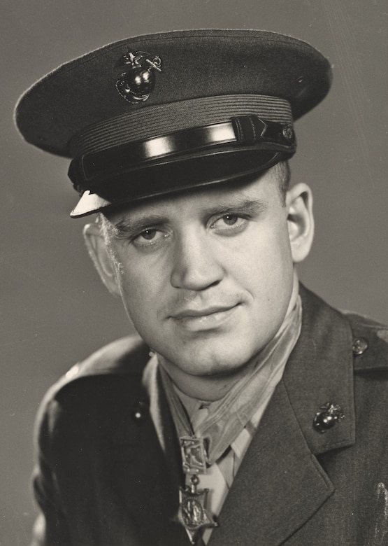 A Marine wearing a dress uniform and a Medal of Honor around his neck looks at the camera.