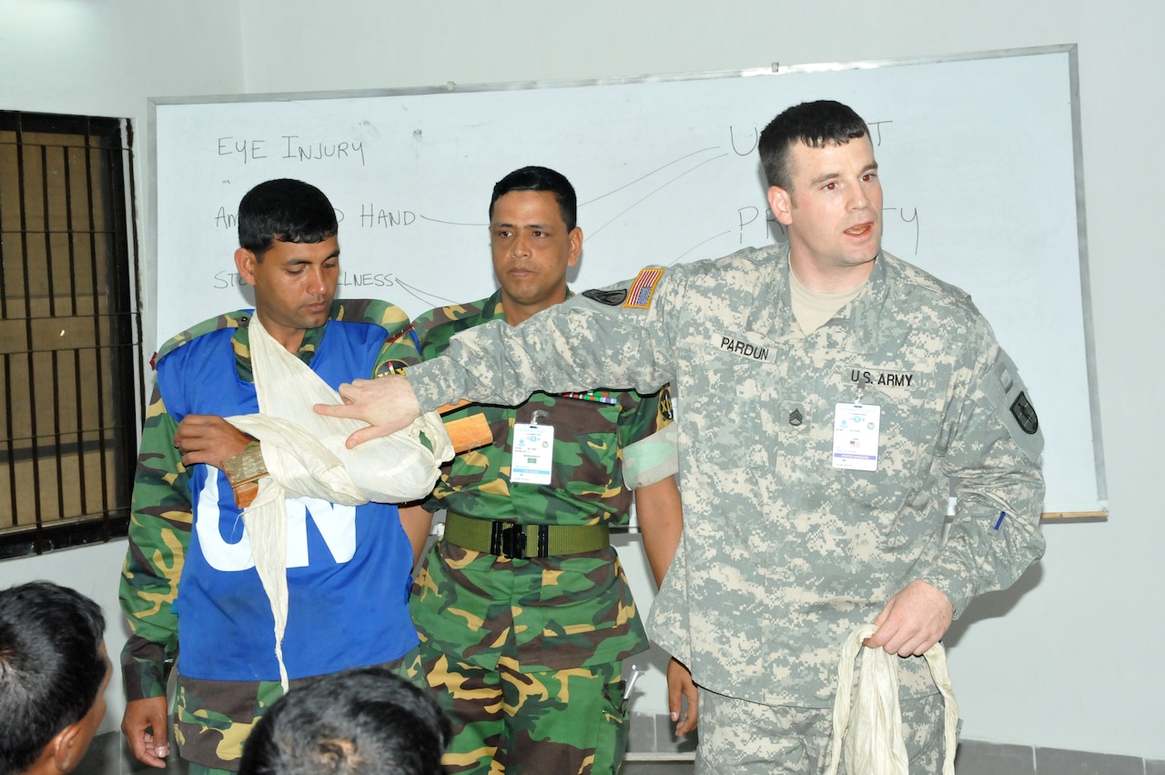 Soldier stands in front of a class and points to a splint on the arm of a man.