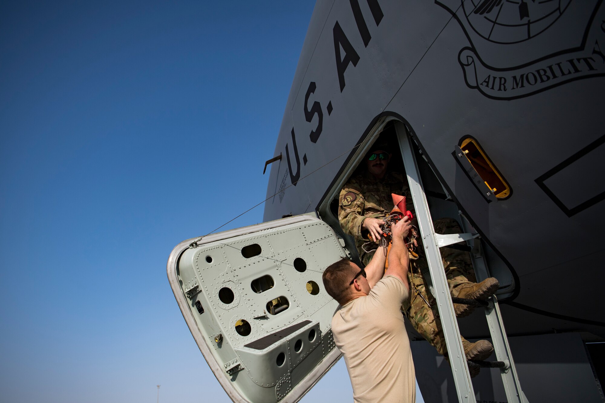 A U.S. Air Force KC-135 Stratotanker crew chief assigned to the 385th Expeditionary Aircraft Maintenance Squadron hands equipment to a U.S. Air Force pilot assigned to the 28th Expeditionary Air Refueling Squadron at Al Udeid Air Base, Qatar, Jan. 3, 2020.