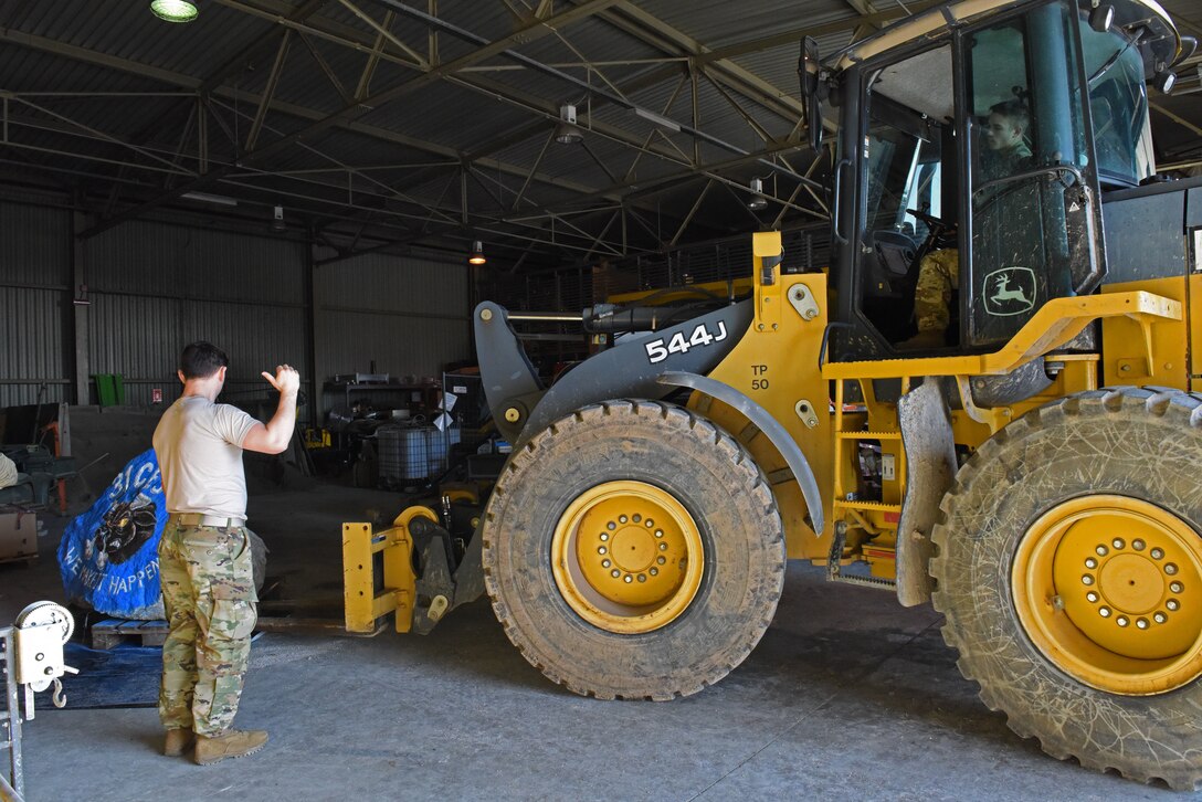 U.S. Air Force Senior Airman Christopher Margotti guides Airman 1st Class Aaron Looker as he operates a forklift to pick up a spirit rock at Aviano Air Base, Italy, Jan. 30, 2020. Both Margotti and Looker are with the 31st Civil Engineer Squadron, which was responsible for painting the rock and placing it in front of the 31st Fighter Wing headquarters building.