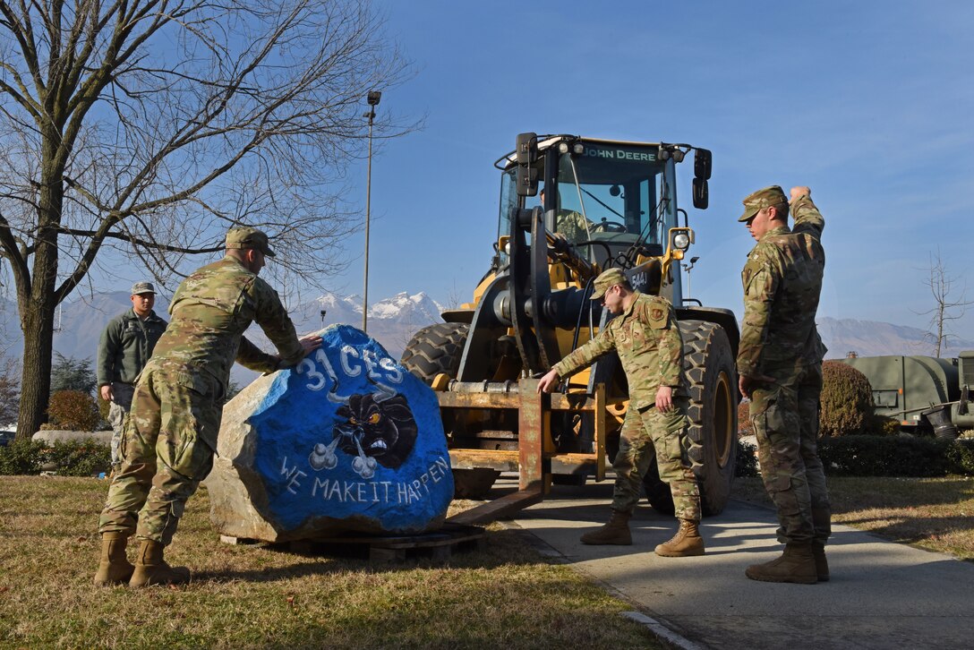 U.S. Airmen from the 31st Civil Engineer Squadron (CES) deliver a spirit rock to the front of the 31st Fighter Wing headquarters building at Aviano Air Base, Italy, Jan. 30, 2020. Capt. William Steers with the 31st CES painted the rock to represent their squadron.