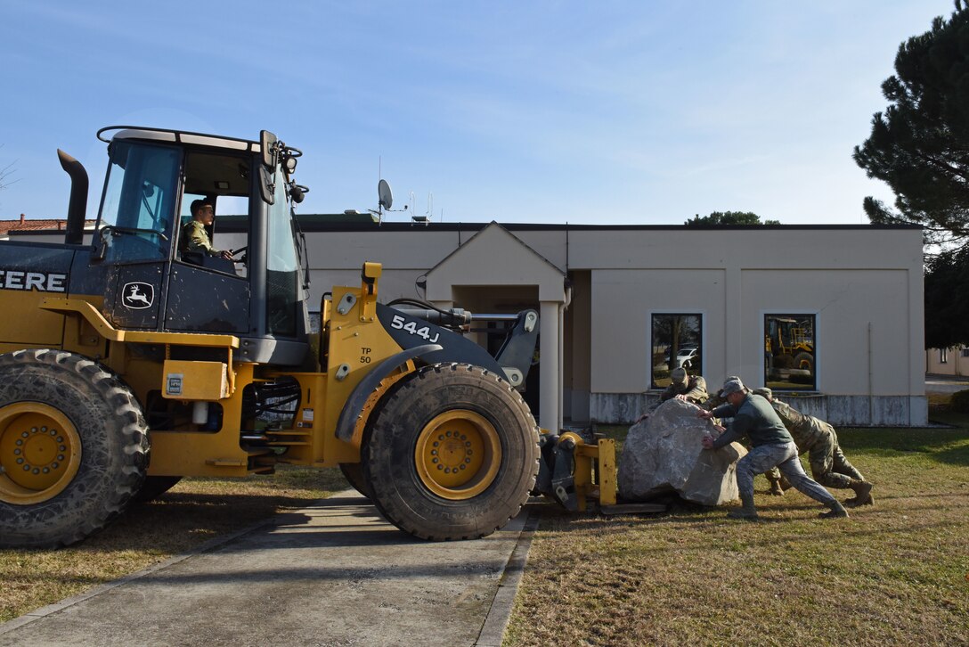 U.S. Airmen from the 31st Civil Engineer Squadron deliver a spirit rock to the front of the 31st Fighter Wing headquarters building at Aviano Air Base, Italy, Jan. 30, 2020. Capt. William Steers with the 31st CES painted the rock to represent their squadron.
