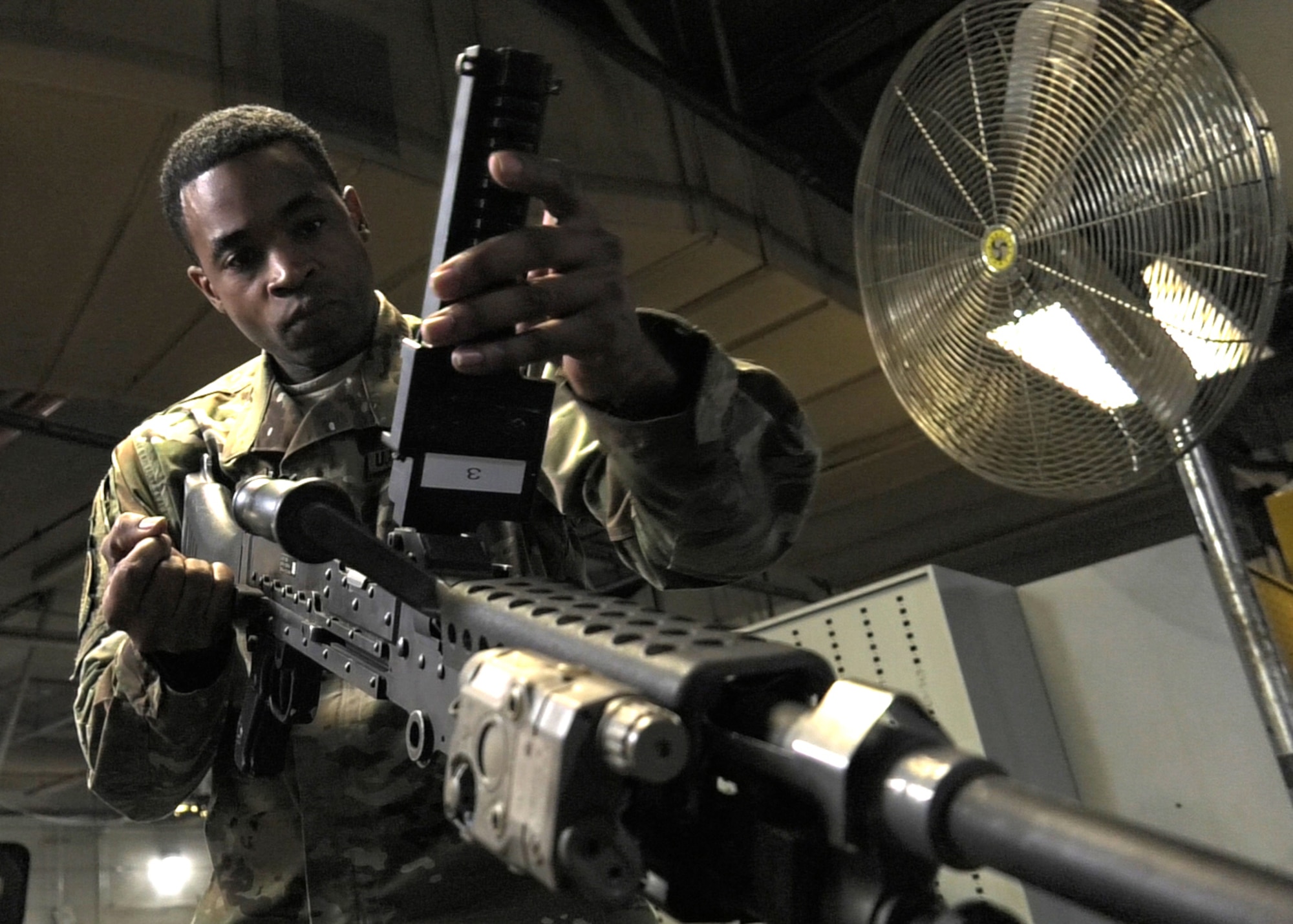 close of photo TSgt. Hamm inspecting weapon for mechanical discrepancies. there is a large circulating fan in the background to the right