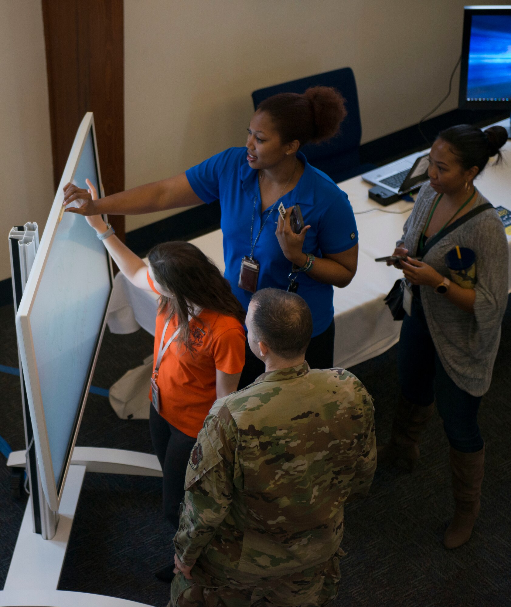 A photograph of people gathered around an electronic whiteboard, smiling.