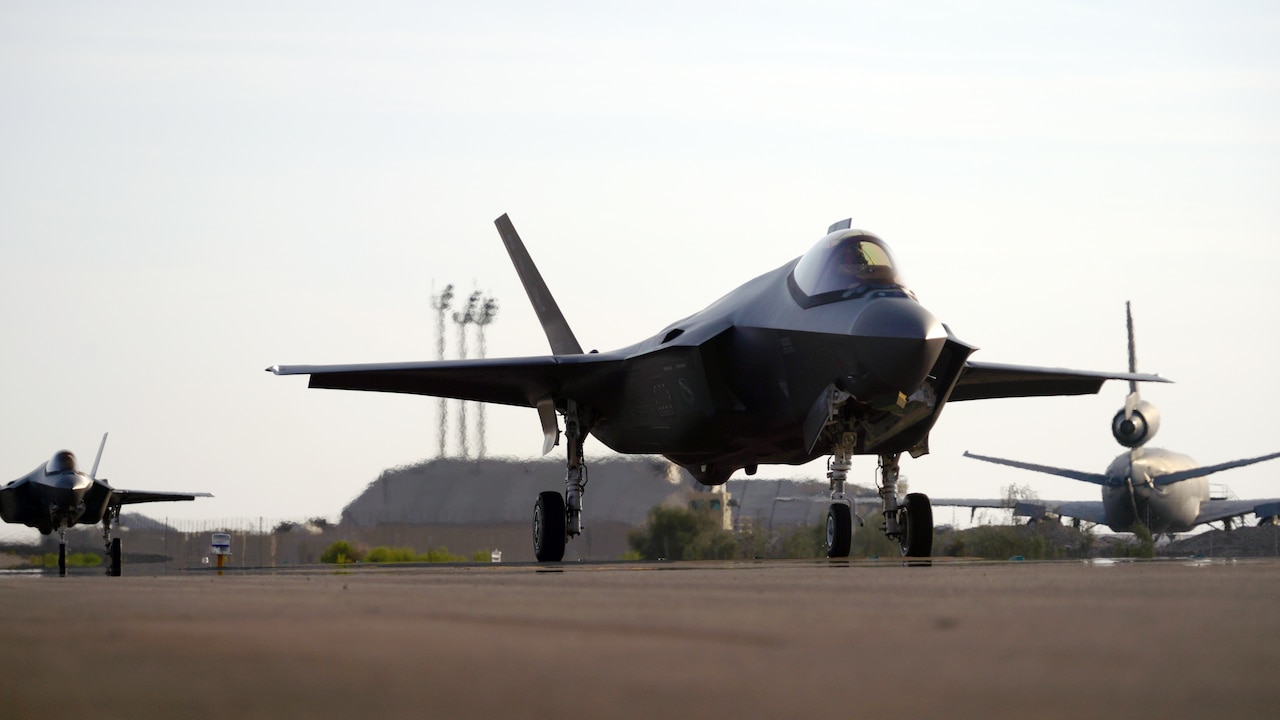 A U.S. military fighter jet sits on a runway near other aircraft.