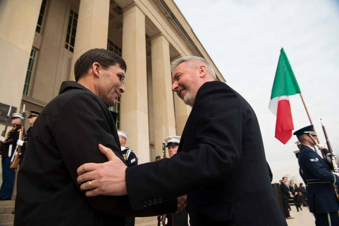 Two men shake hands with one grasping the other’s arm..
