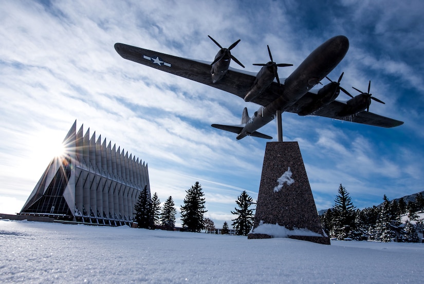 Static shot of a vintage aircraft at the top of a pedestal with the U.S. Air Force Academy chapel in the background.