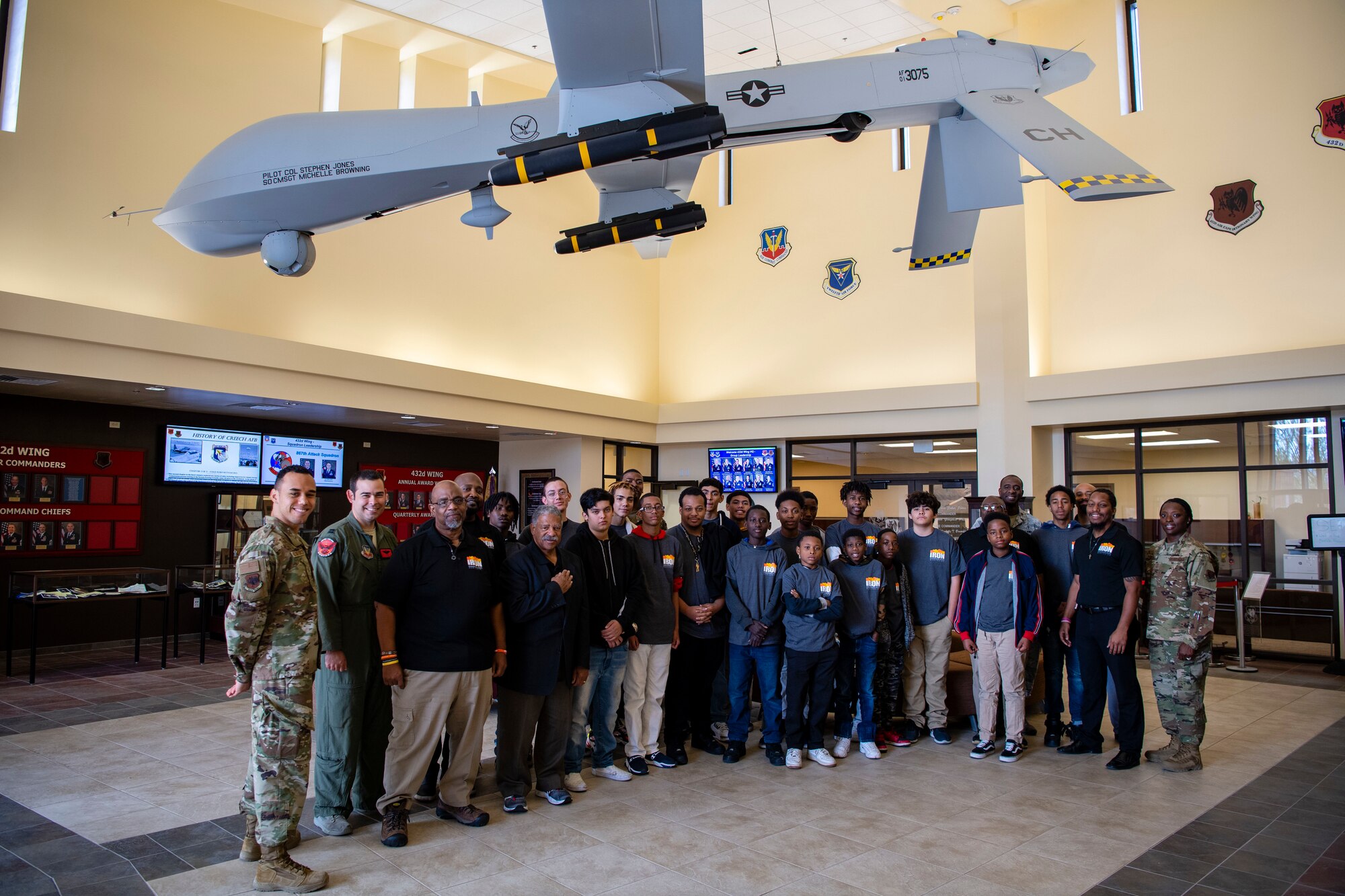 432nd Wing/432nd Air Expeditionary Wing Airmen members, Iron Sharpens Iron Mentoring youth and mentors take a group photo under an MQ-1 Predator during their visit to Creech Air Force Base