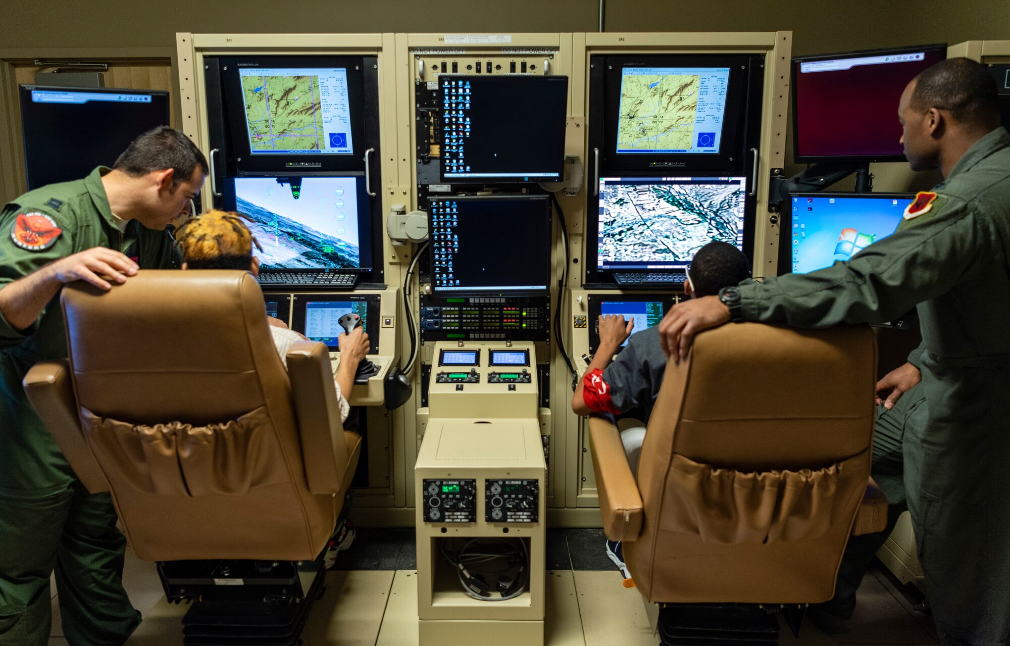 Capt. Marcus, left, 432nd Wing executive officer, and Lt. Col.  Michawn, right, 17th Attack Squadron director of operations, teach local youth as they sit in the pilot’s seat of an MQ-9 Reaper in a flight simulator at Creech Air Force Base
