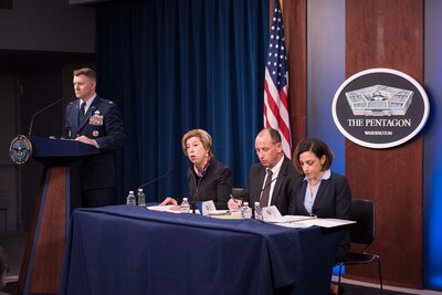 Three people sit behind a table and speak to reporters.