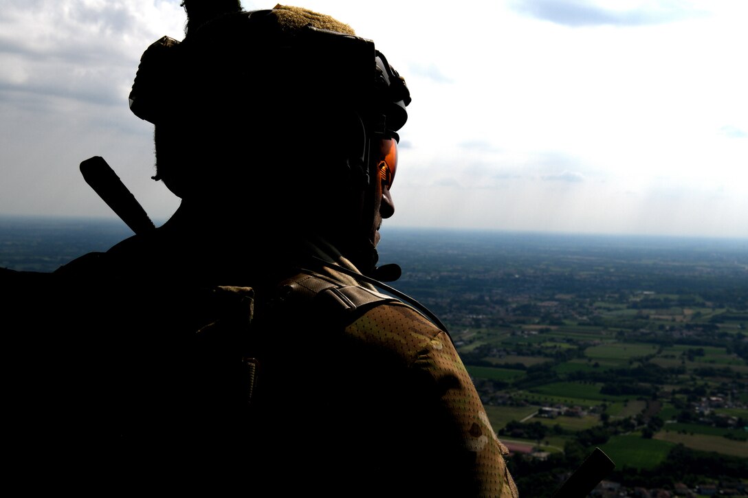 A pararescueman from the 57th Rescue Squadron looks out of an HH-60G Pave Hawk during Operation Porcupine over a military training area in Osoppo, Italy, June 30, 2020. Operation Porcupine demonstrated the unique capabilities of the 31st Operations Group which host all assets needed to conduct a combat search and rescue mission. (U.S. Air Force photo by Senior Airman Caleb House)