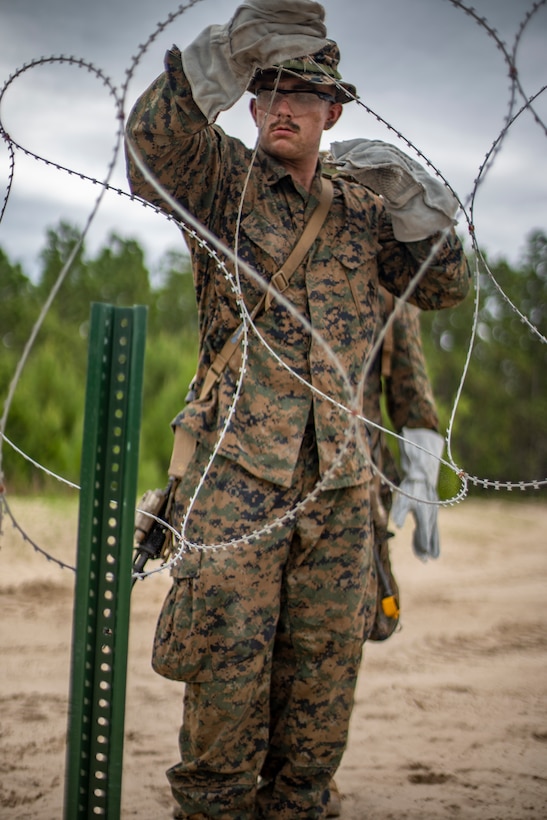 Lance Cpl. Vance Miller, a combat engineer with Special Purpose Marine Air-Ground Task Force - Southern Command, builds a barbed wire defense position during a field exercise at Camp Lejeune, North Carolina, June 9, 2020. The FEX provides the Marines and Sailors the opportunity to stay proficient with their equipment and refine their tactical skill sets. SPMAGTF-SC is poised to conduct crisis response, general engineering training and theater security cooperations alongside partner nation militaries in Latin America and the Caribbean. Miller is a native of Salem, Oregon. (U.S. Marine Corps photo by Sgt. Andy O. Martinez)