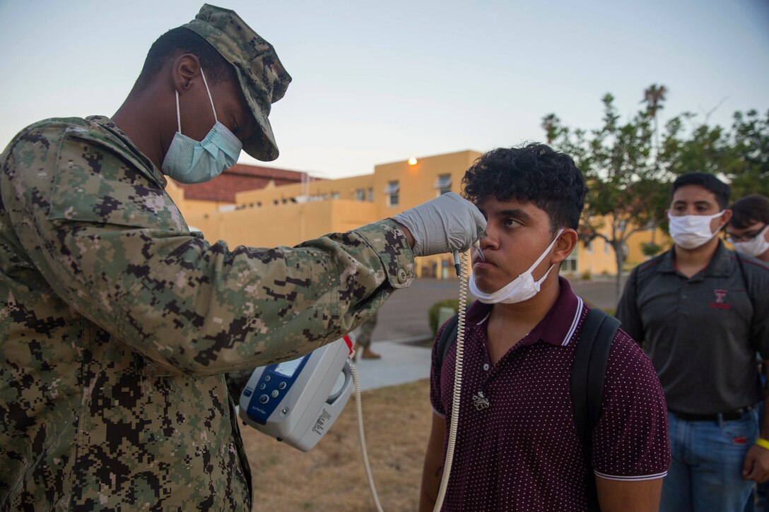 A service member takes the temperature of a Marine Corps recruit.