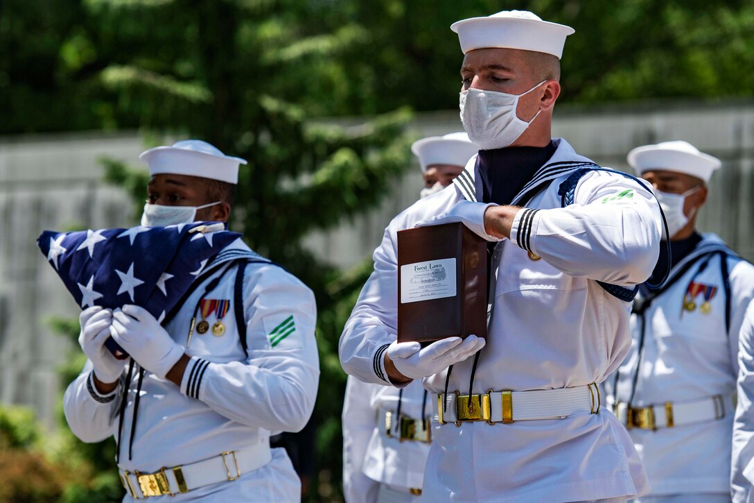 Sailors wearing masks and gloves conduct military funeral honors.