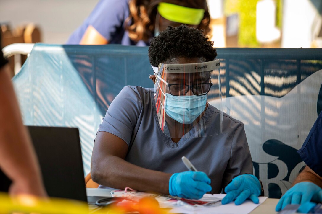 A soldier wearing personal protective equipment works at a walk-up registration table.