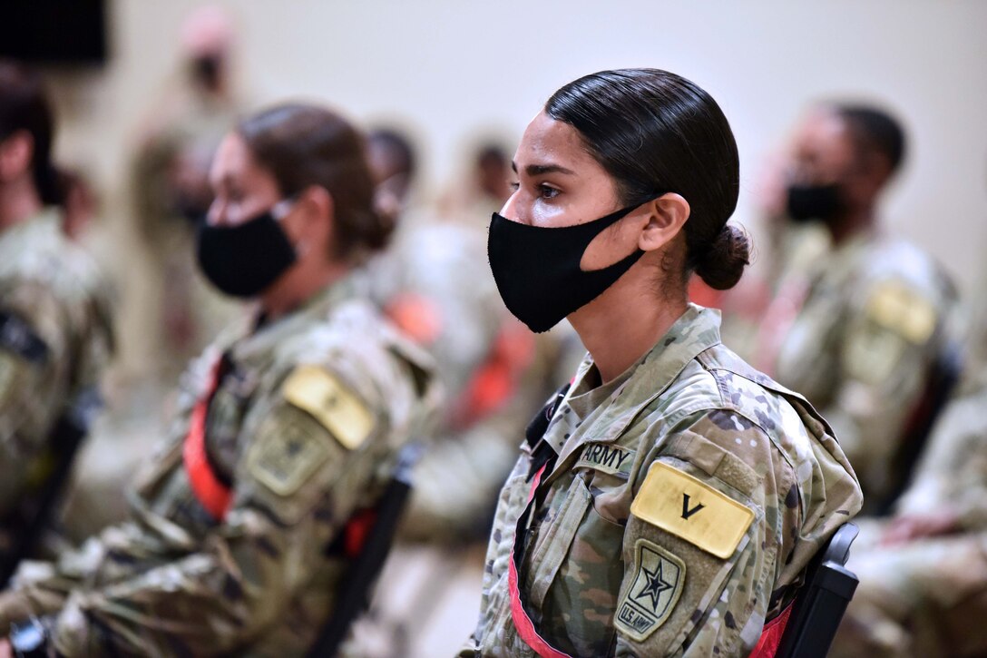 Several soldiers wearing masks listen to a senior officer during a forum.