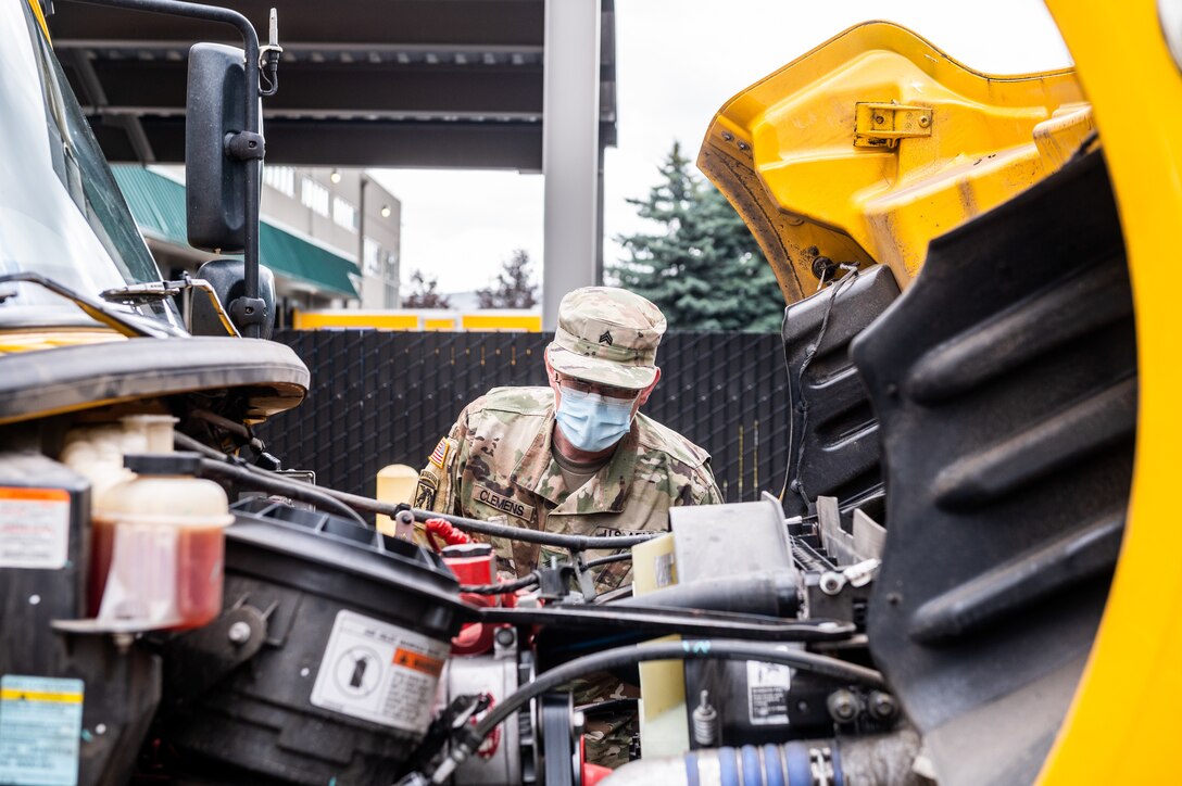 A soldier checks under the hood of a truck.