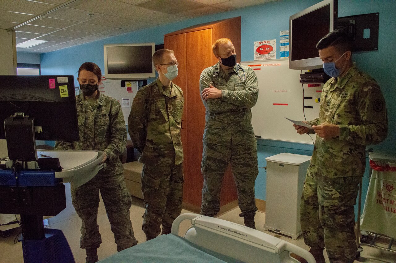 Four military doctors wearing masks stand in a pediatrics ward as one of them checks a monitor.