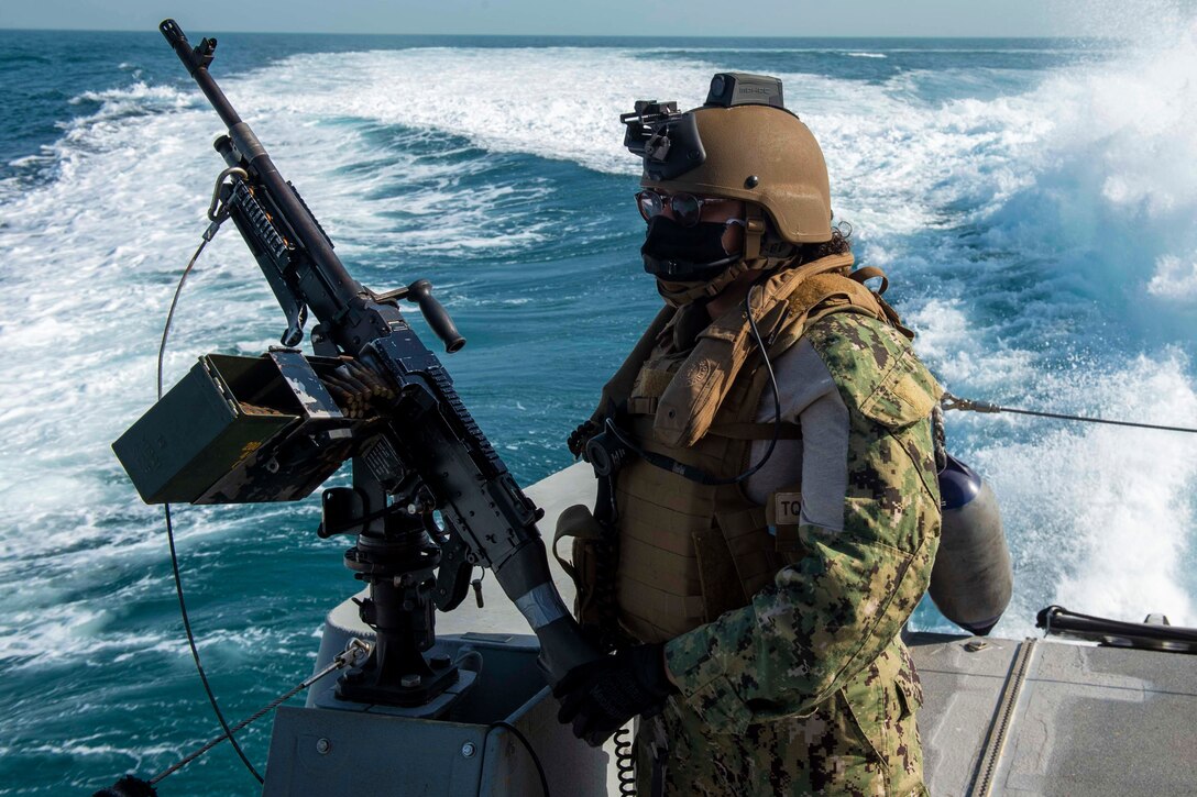 A sailor stands by a machine gun on a boat.