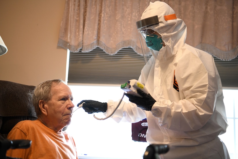 An airman wearing full protective gear takes the temperature of a COVID-19 patient.