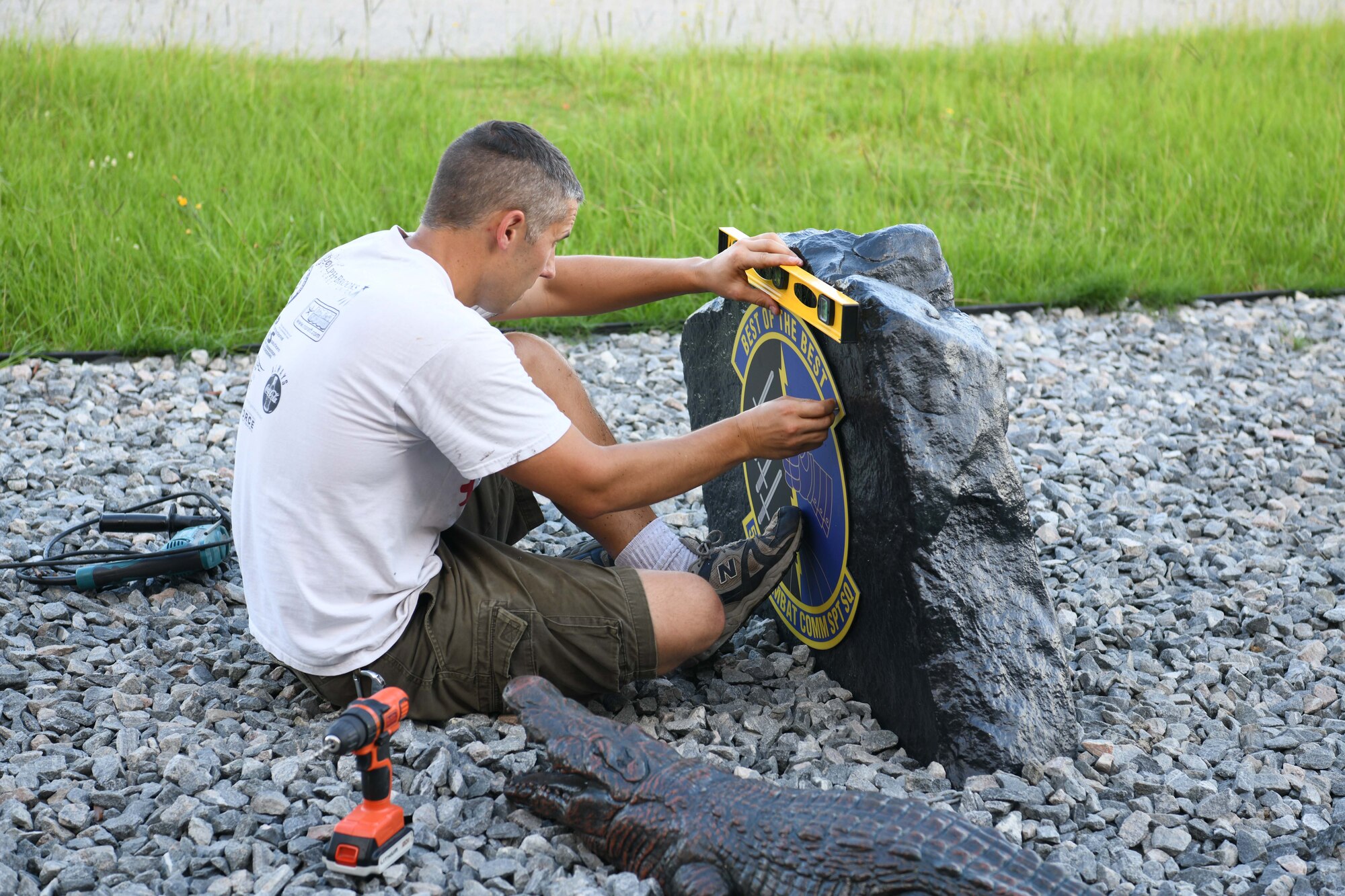 Photo shows a person with a leveler straitening a sign against a boulder.