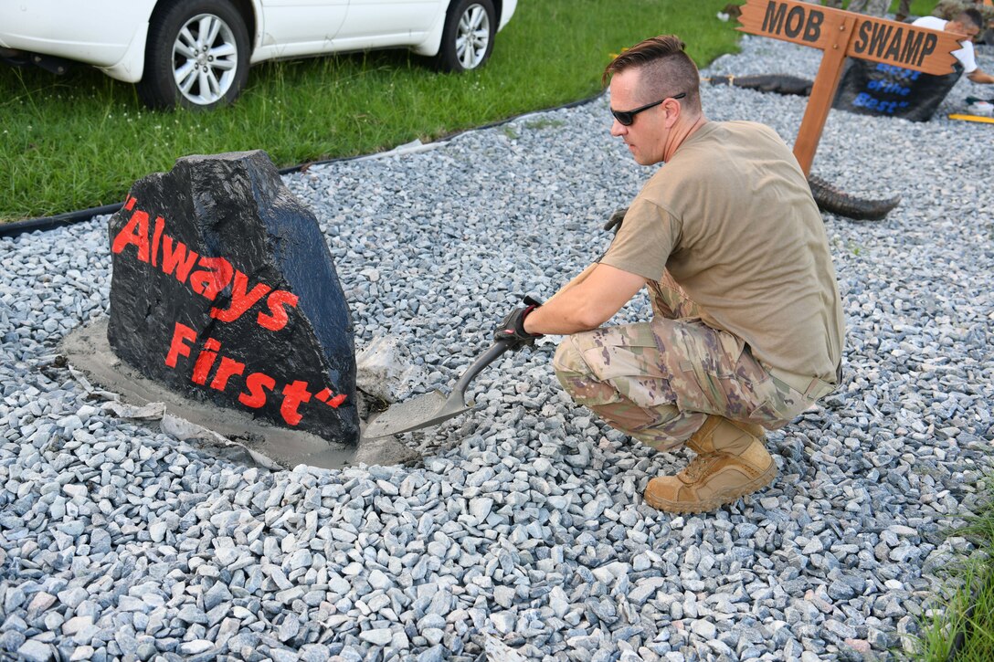 Photo shows an Airmen shoveling cement around a boulder.
