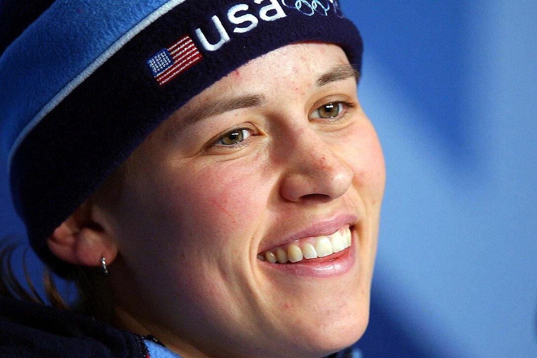 An athlete wearing a winter cap with an American flag on it smiles.