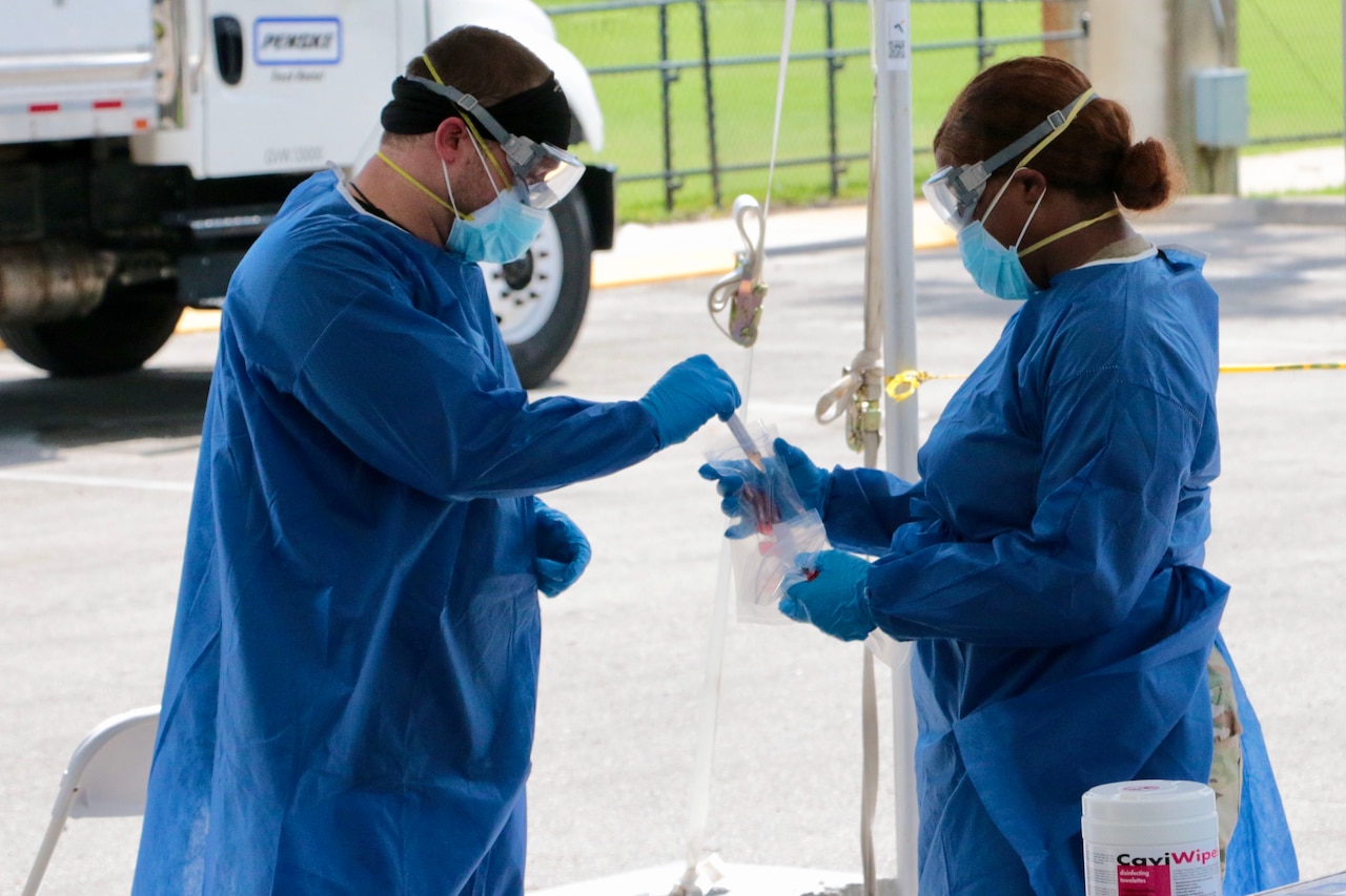 A soldier holds a plastic bag open as a health care provider deposits a nasal swab into it.