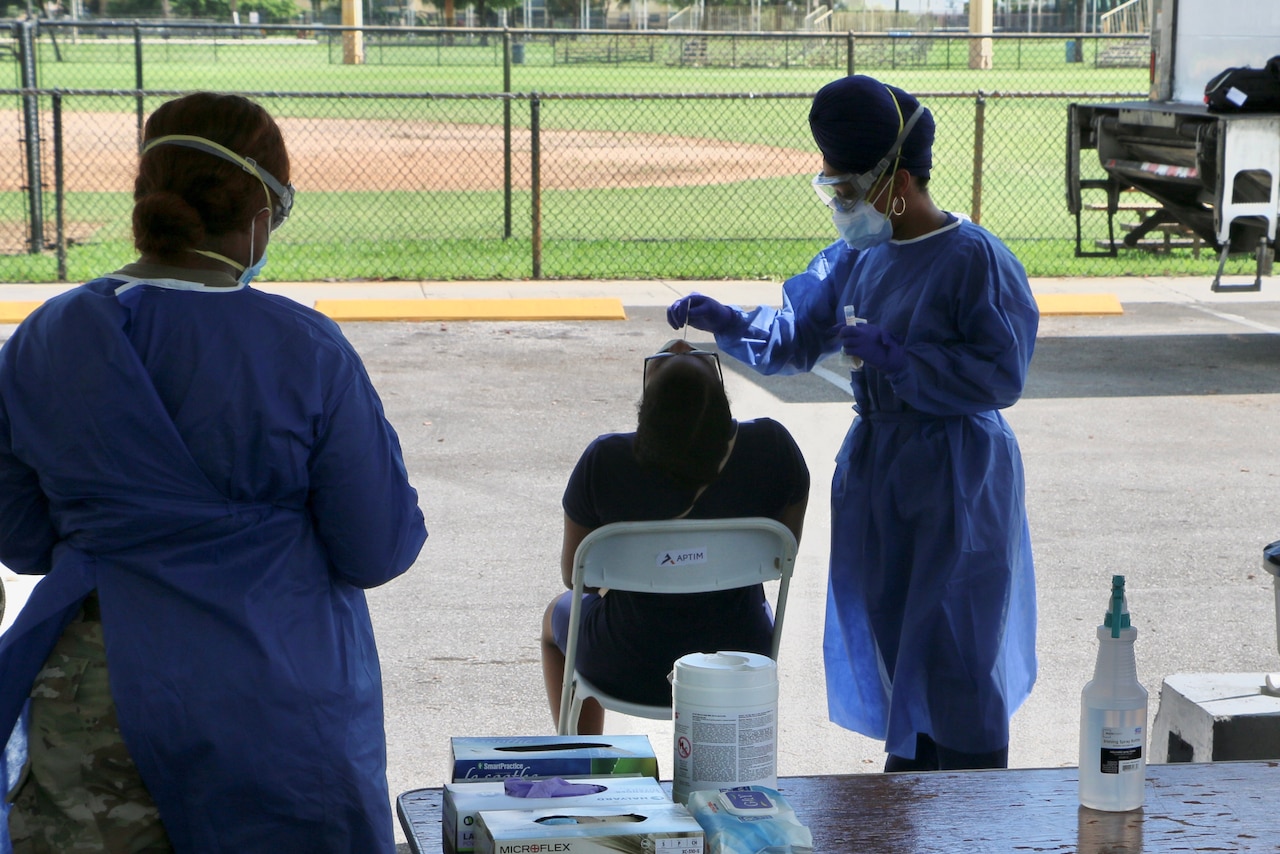 A soldier assists with  a nasal-swab specimen collection.