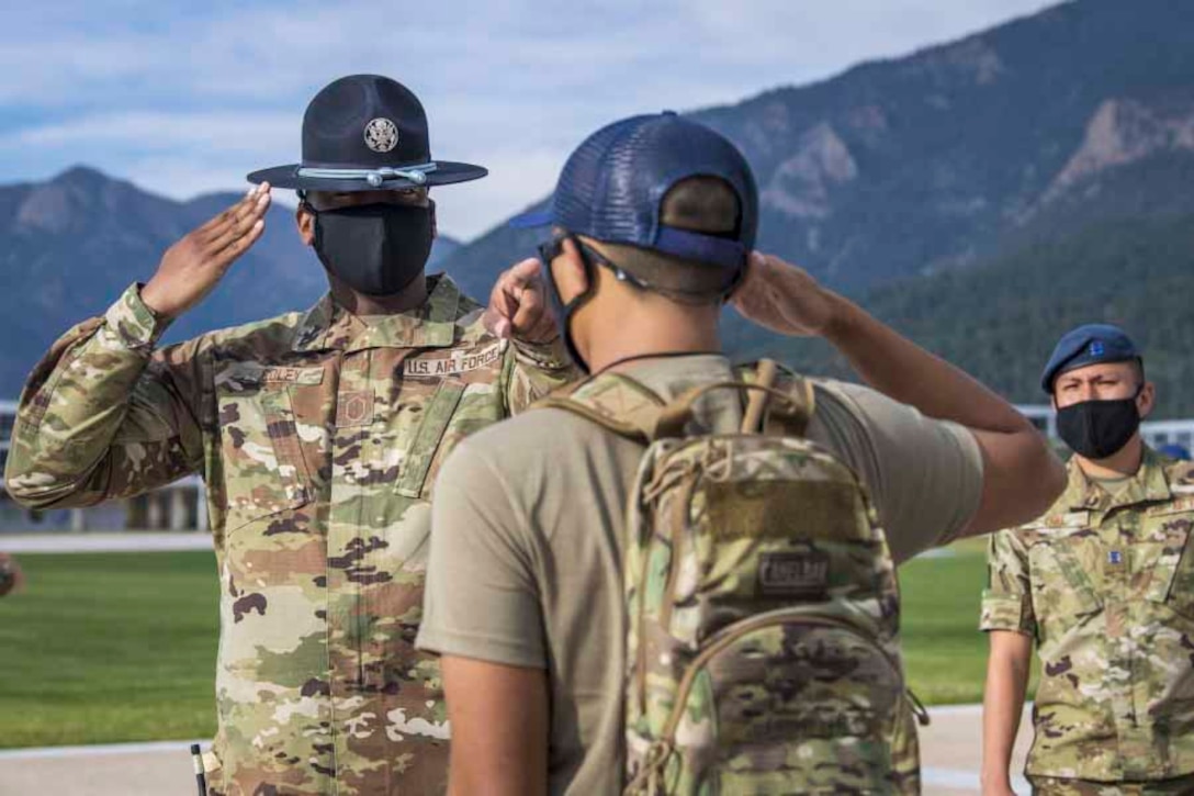 An airman salutes a cadet as another airman stands to the side; all three wear face masks.