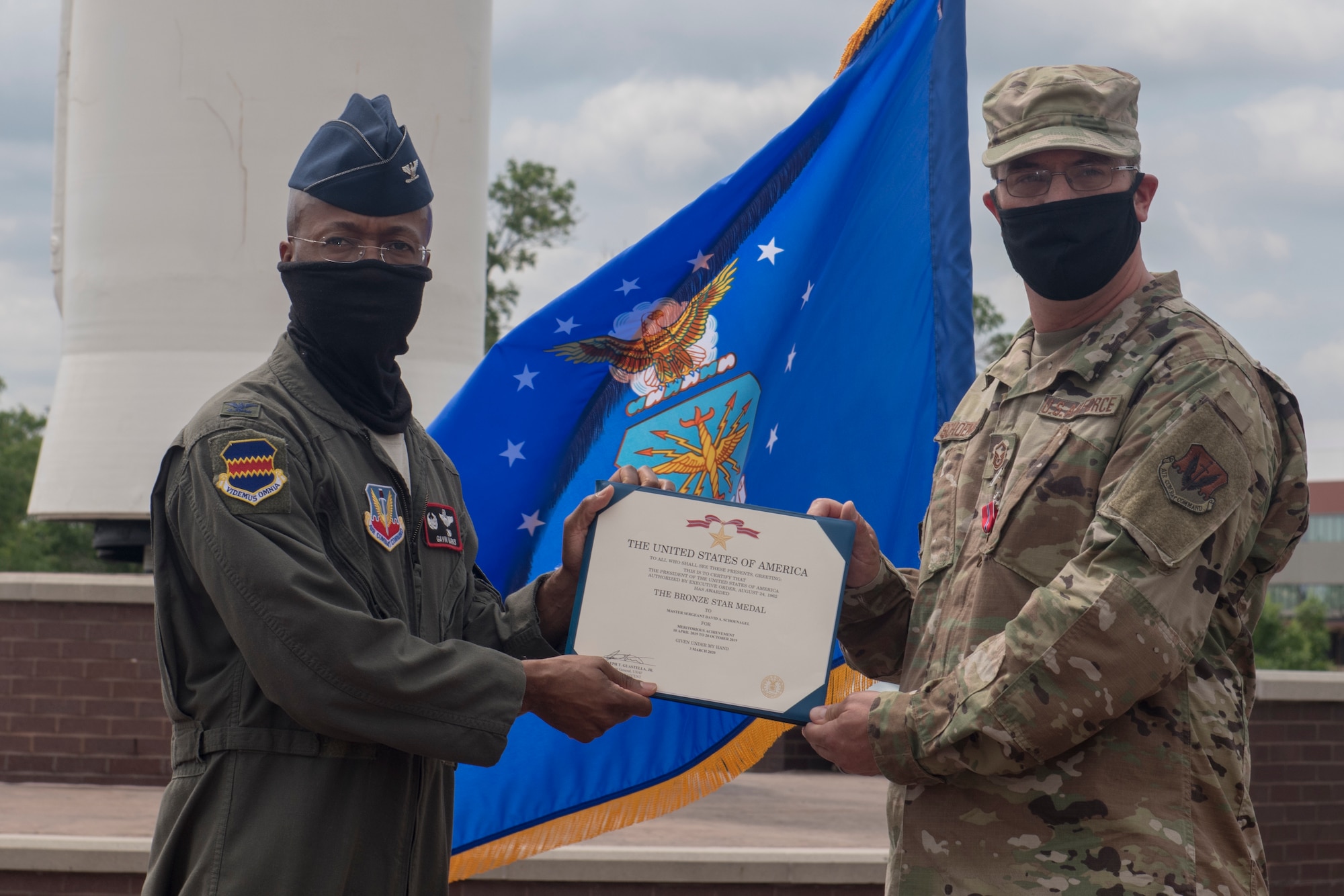 service member in flight suit presents service member in OCPs with Bronze Star Medal certificate.
