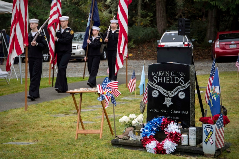 A military honor guard carries the American and Navy flags during a ceremony at a cemetery.