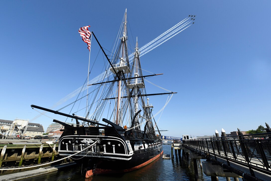 A group of military aircraft fly above an old ship.