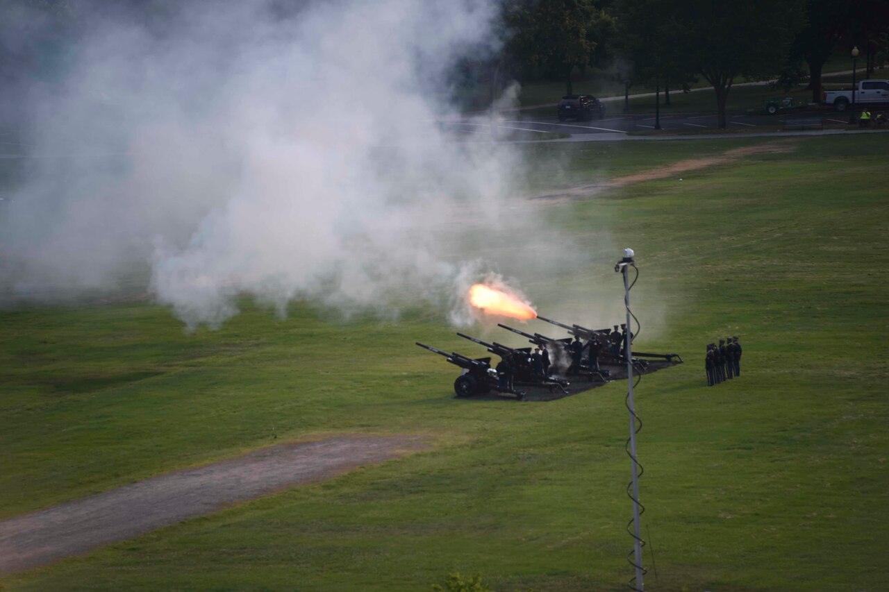Military service members fire a cannon on a large lawn.