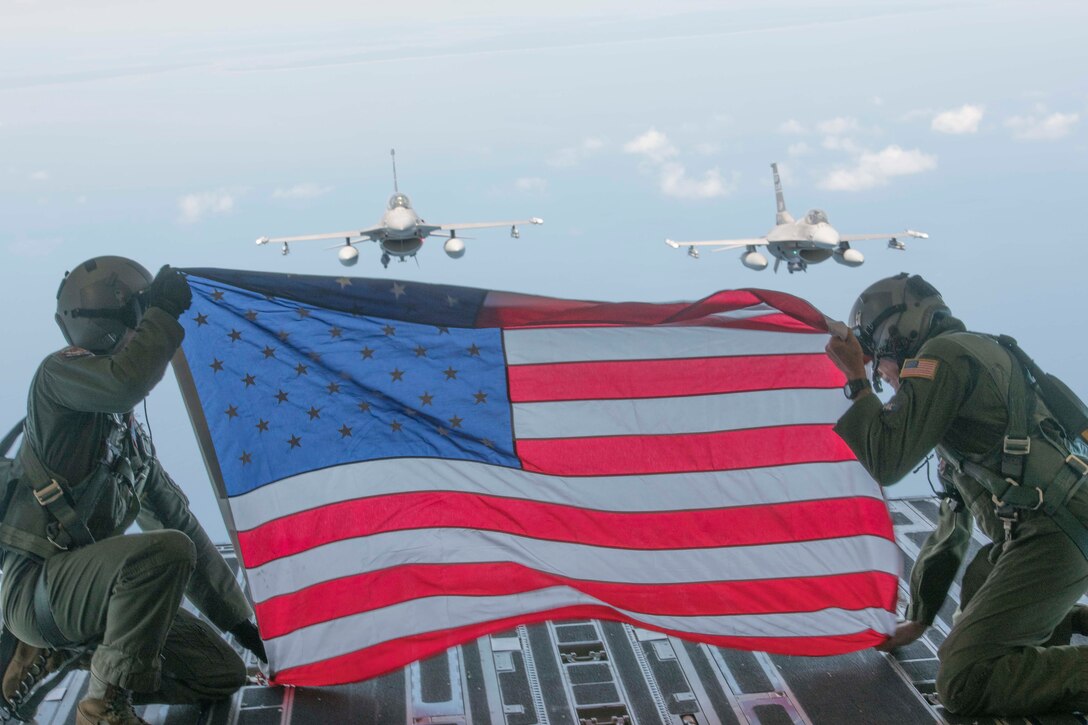 Members of Team Charleston hold the flag up in honor of fallen Air Force Hero 1st Lt. David Schmitz, pilot, 77th Fighter Squadron, Shaw Air Force Base on July 4, 2020 at Joint Base Charleston, S.C. Two F-16 Fighting Falcons from The 169th Fighter Wing, McEntire Joint National Guard Base flew in formation behind the C-17 Globemaster III.