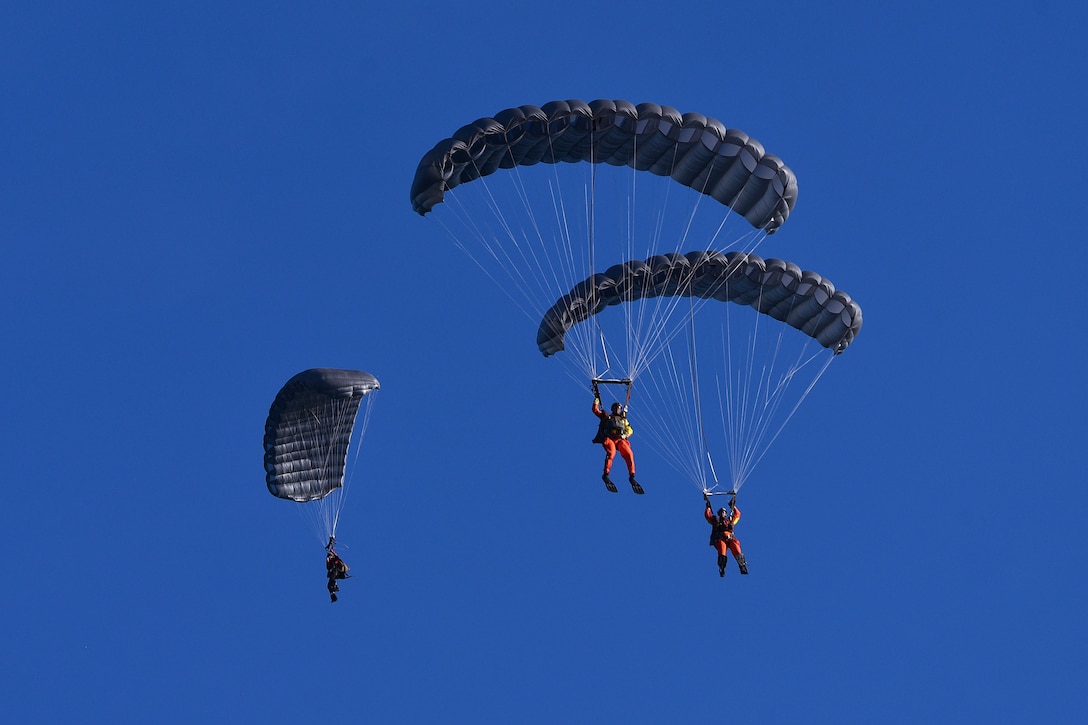 Three airmen with parachutes freefall next to one another.