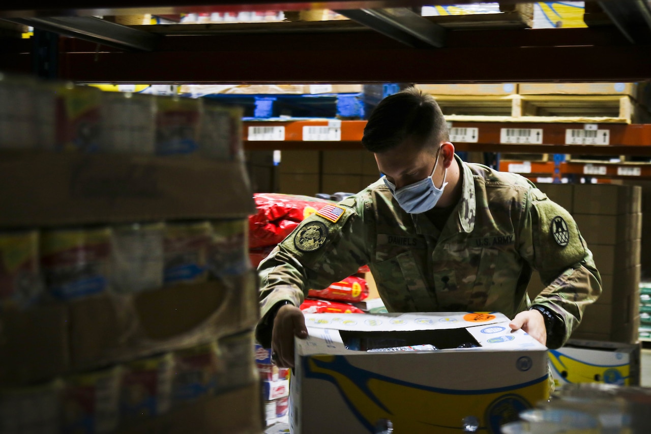 A soldier places boxes of food onto a pallet at a food bank.