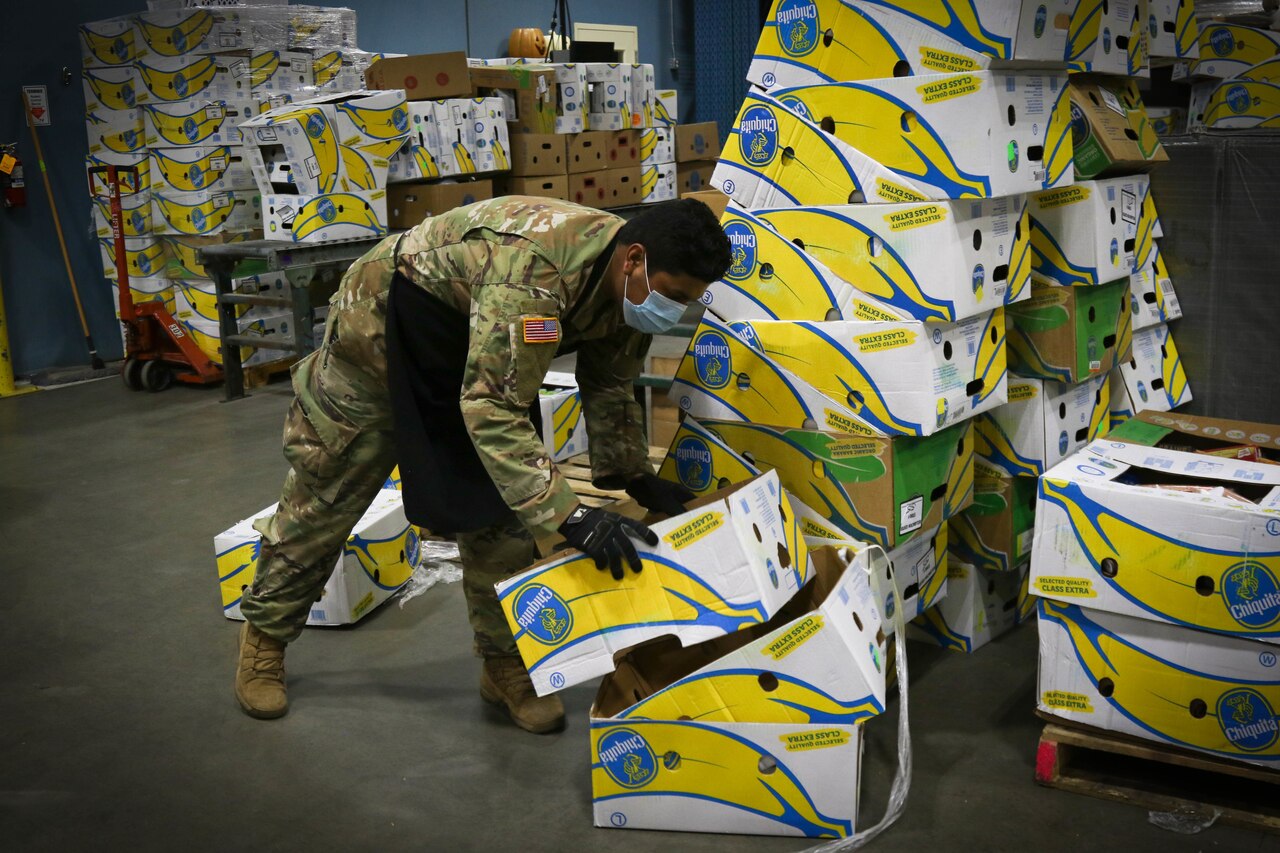 A soldier sorts cardboard boxes at a food bank.