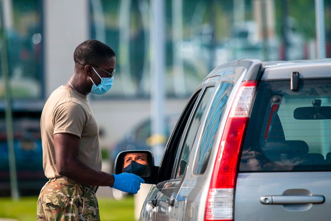 A soldier wearing personal protective equipment talks to a person sitting inside of a vehicle.