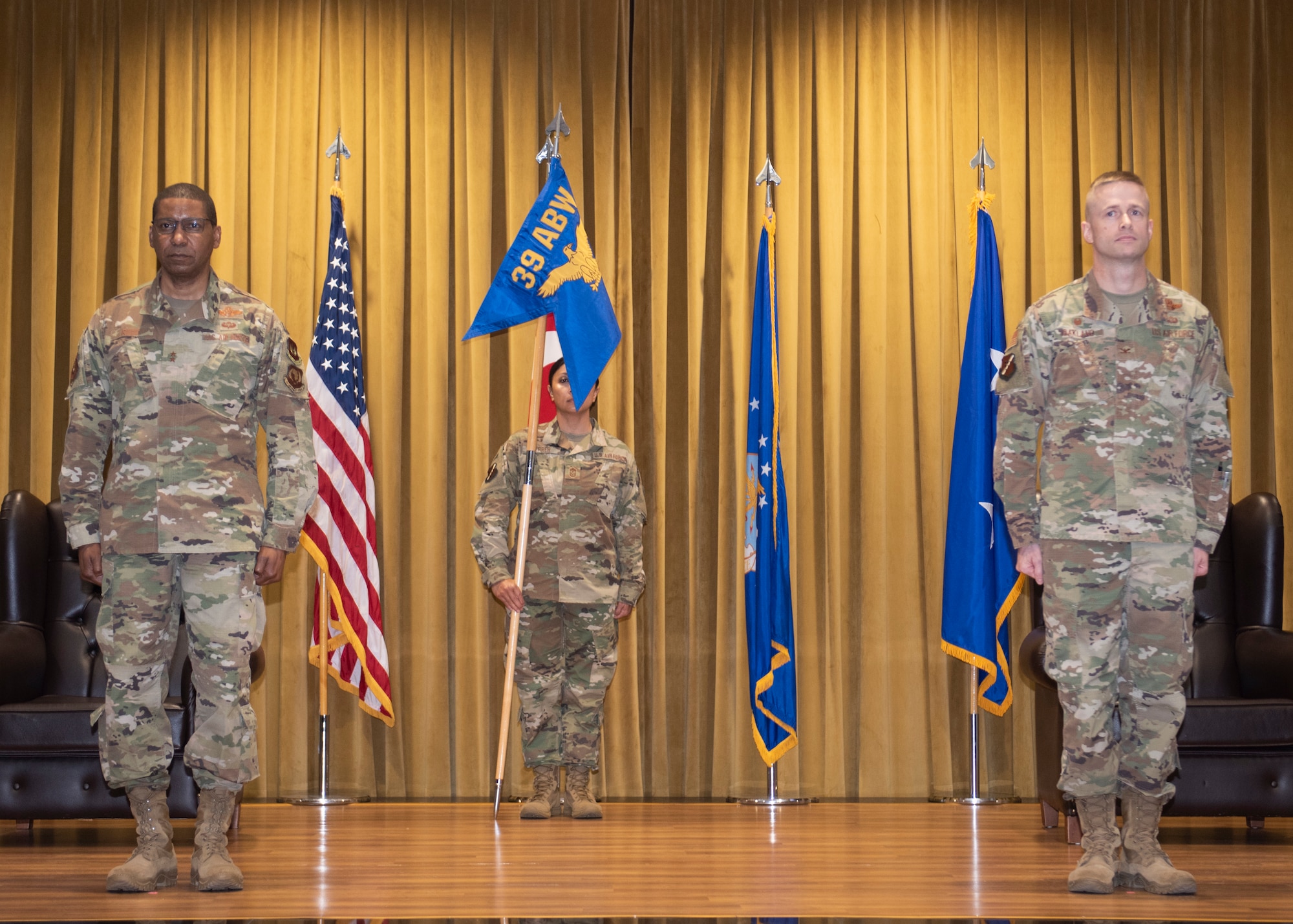 Photo of three Airmen standing on stage at a change of command