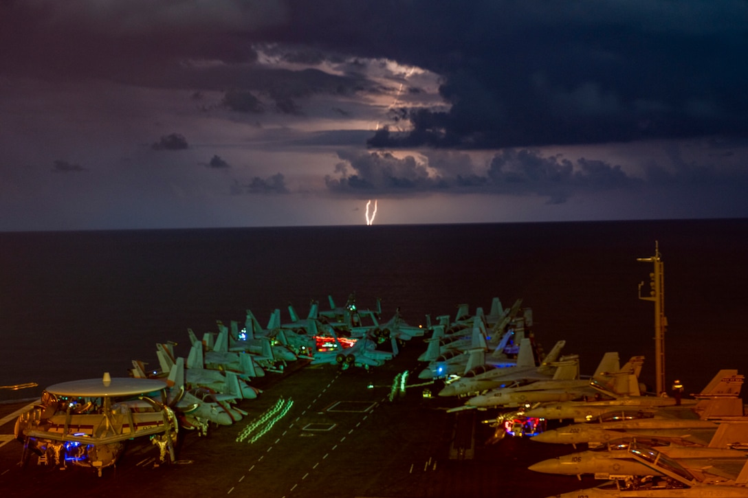 A lightning flash at night lights up aircraft on a military ship.