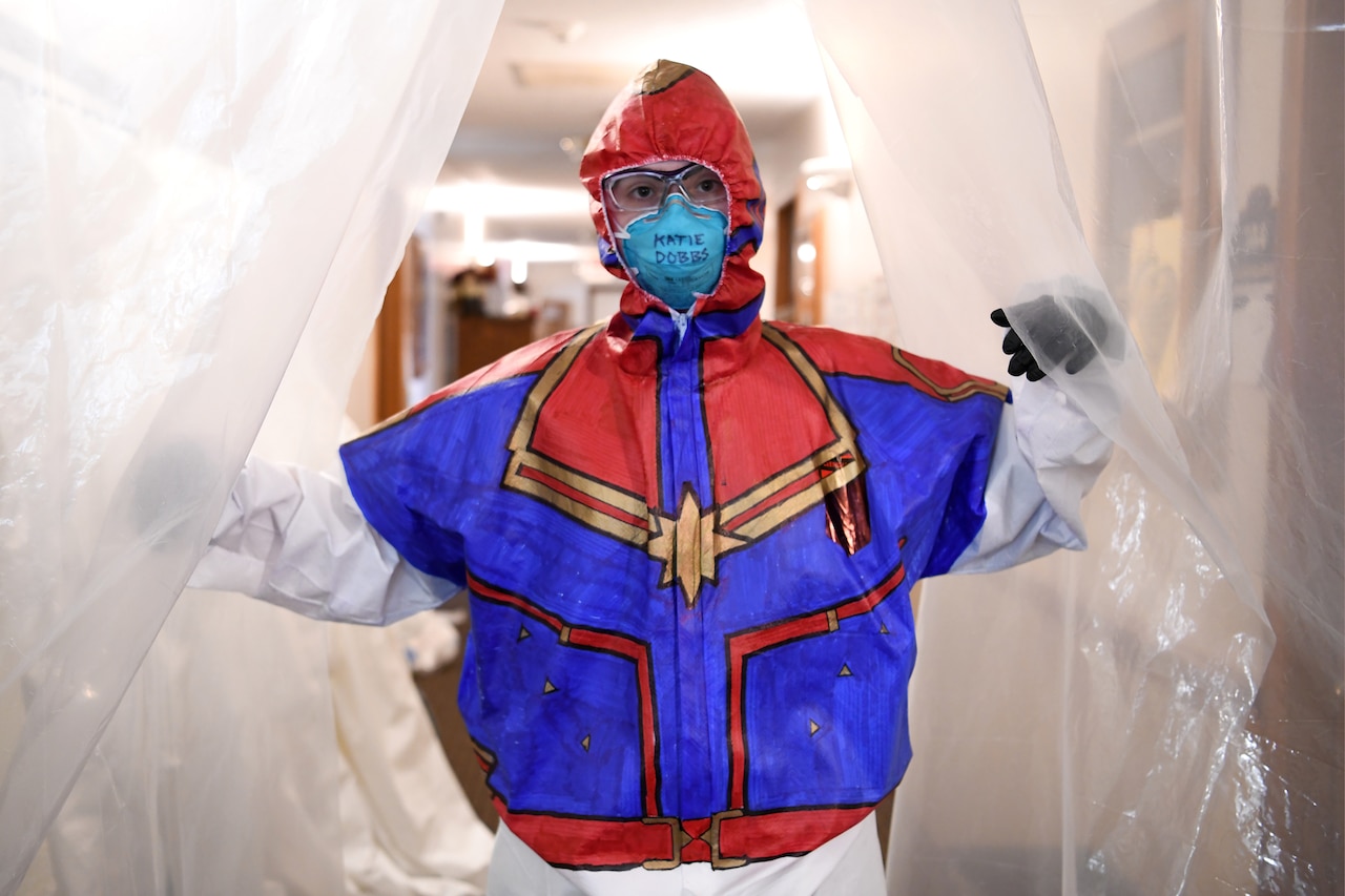 An airman wearing a superhero-inspired protective suit passes through a makeshift doorway made with plastic sheeting.