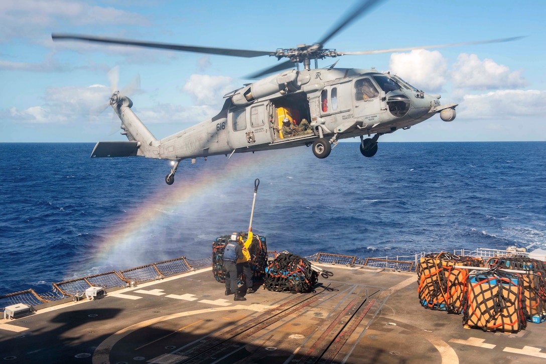 Two sailors attach cargo to a helicopter on a ship in the ocean.