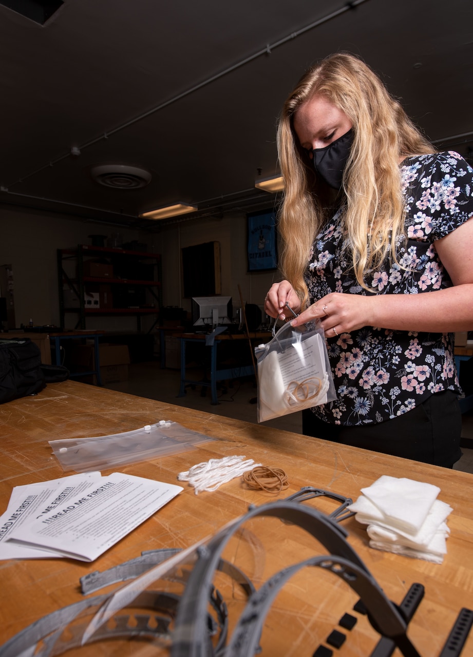 A woman wearing a mask puts 3D-printed personal protective equipment components into plastic bags.