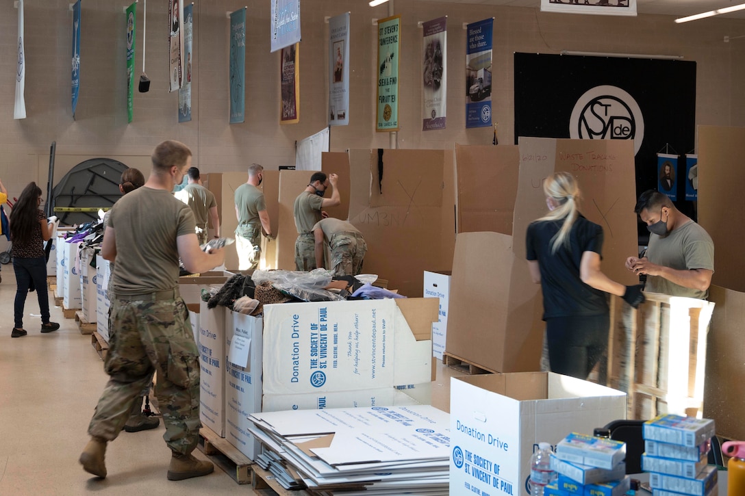 Guardsmen in protective gear sort through boxes.